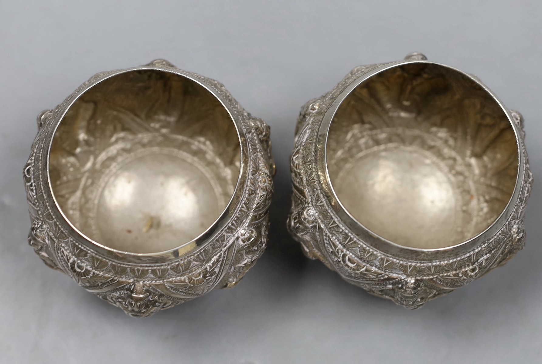 A pair of Indian embossed white metal circular bowls, on three hoof feet, height 82mm.
